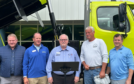 The image shows an open house and facility announcement event at R/S-Godwin (part of The Godwin Group) featuring a bright yellow dump truck in the background.