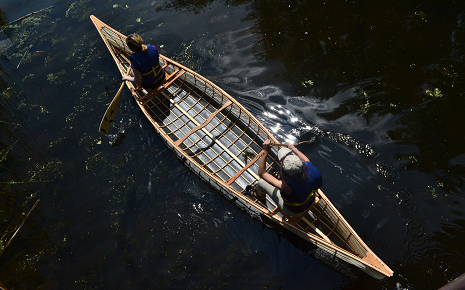 The image shows a birds-eye view of a lightweight canoe  with two paddlers on dark water.