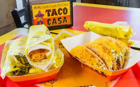 The image shows a spread of fast-food Tex-Mex meals from Taco Casa, featuring items like crunchy tacos, soft tacos, and burritos.
