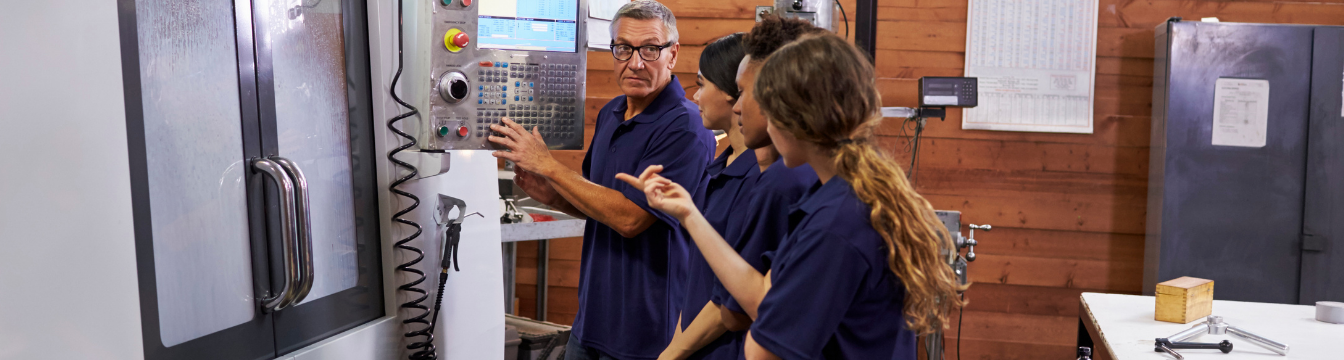 teacher and three students in blue polo shirts working on electronic equipment