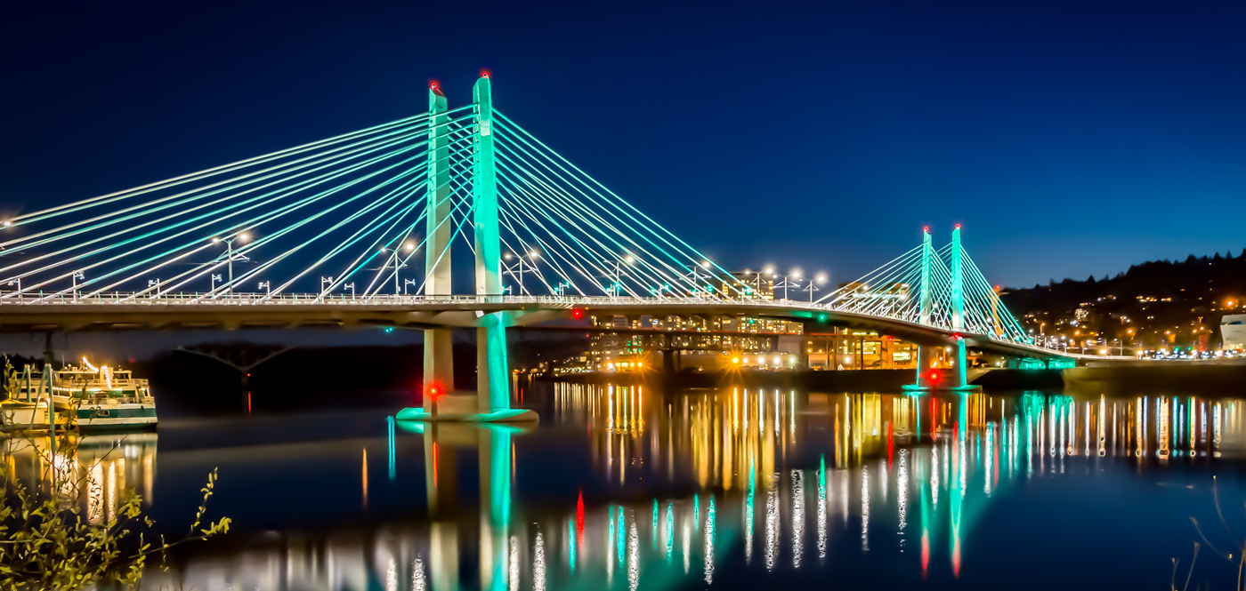 The Tilikum Crossing Bridge, an iconic structure in the Portland Region, light up and night with lights reflecting off of the water.