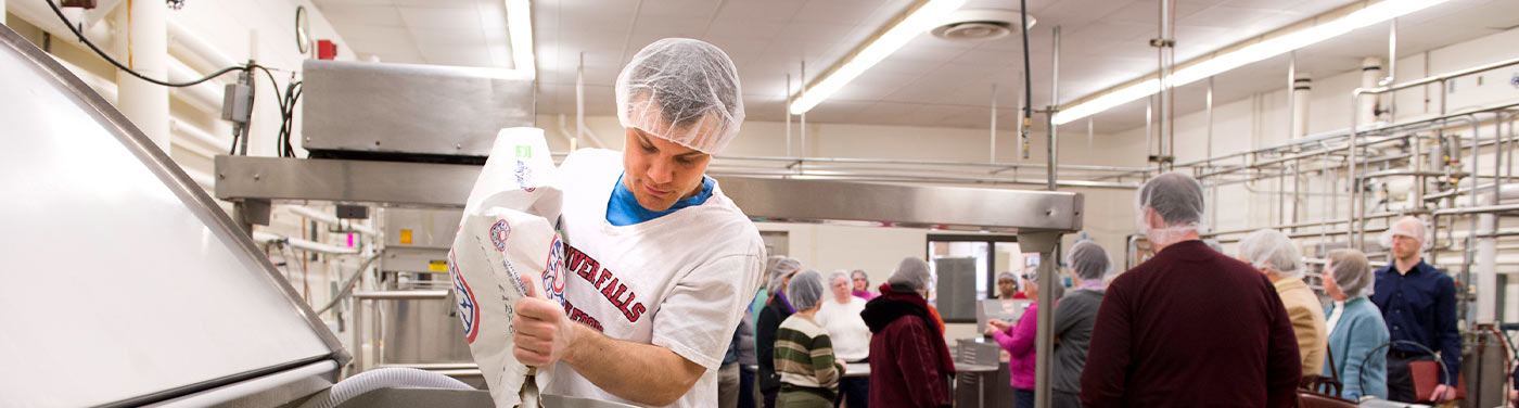 employee training group and man in hairnet pouring sugar into vat