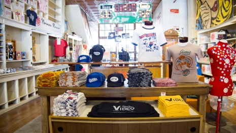 small apparel business interior with hats and shirts with logos and slogans arranged neatly on a table and a variety of shelves.