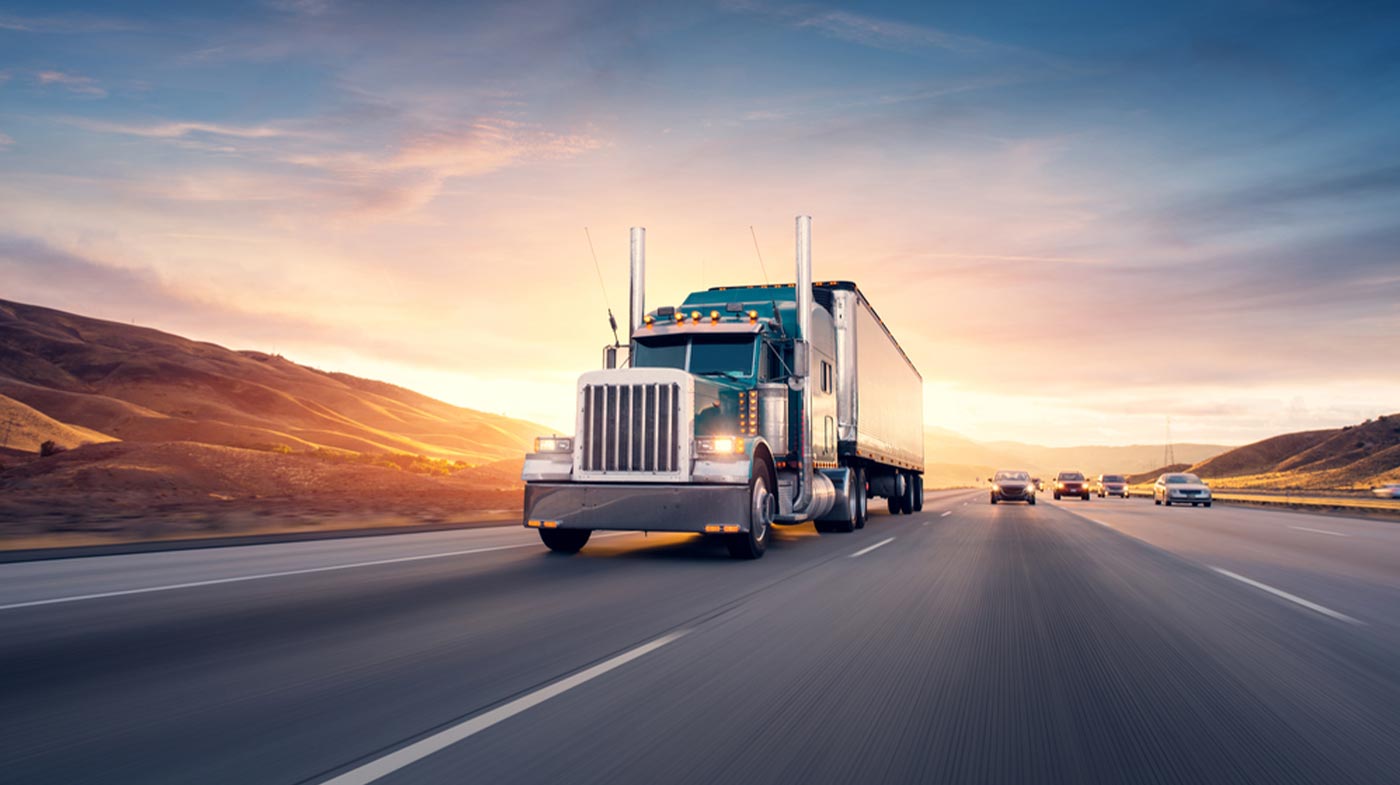 semi-truck driving on road up hill with cars behind