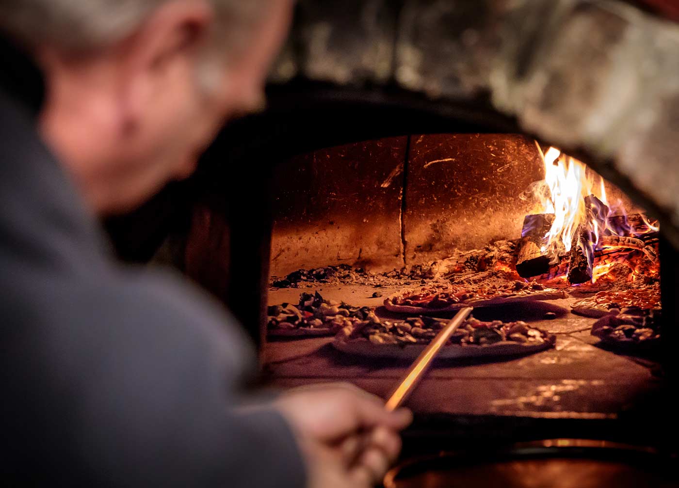 pizza man placing a pizza in a woodfired oven