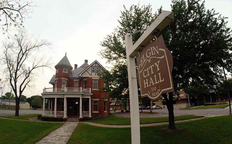 Elgin city hall signpost with city hall building in the background in late Spring.