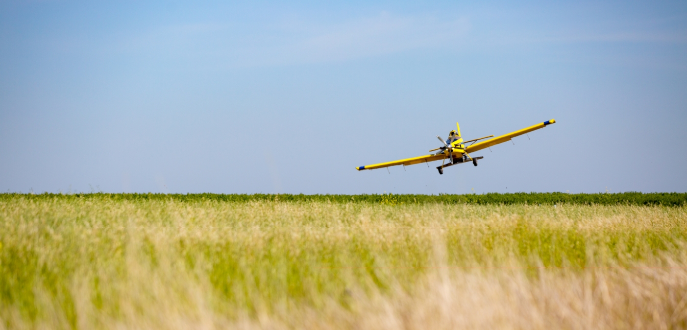 crop duster flying over green and gold fields