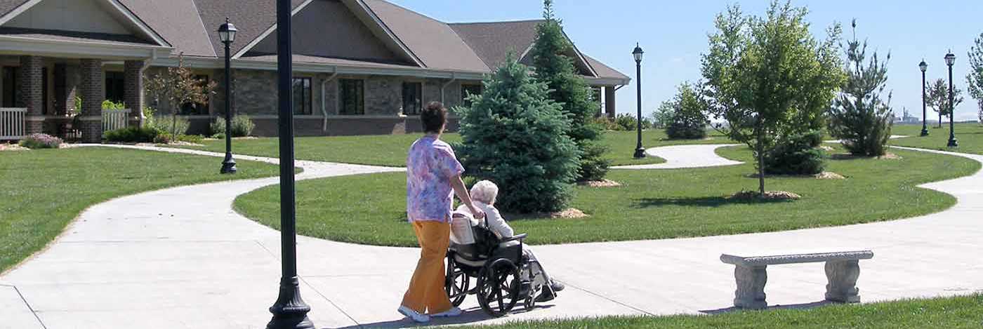 Health aide pushing senior woman in a wheelchair along outdoor paths of healthcare facility