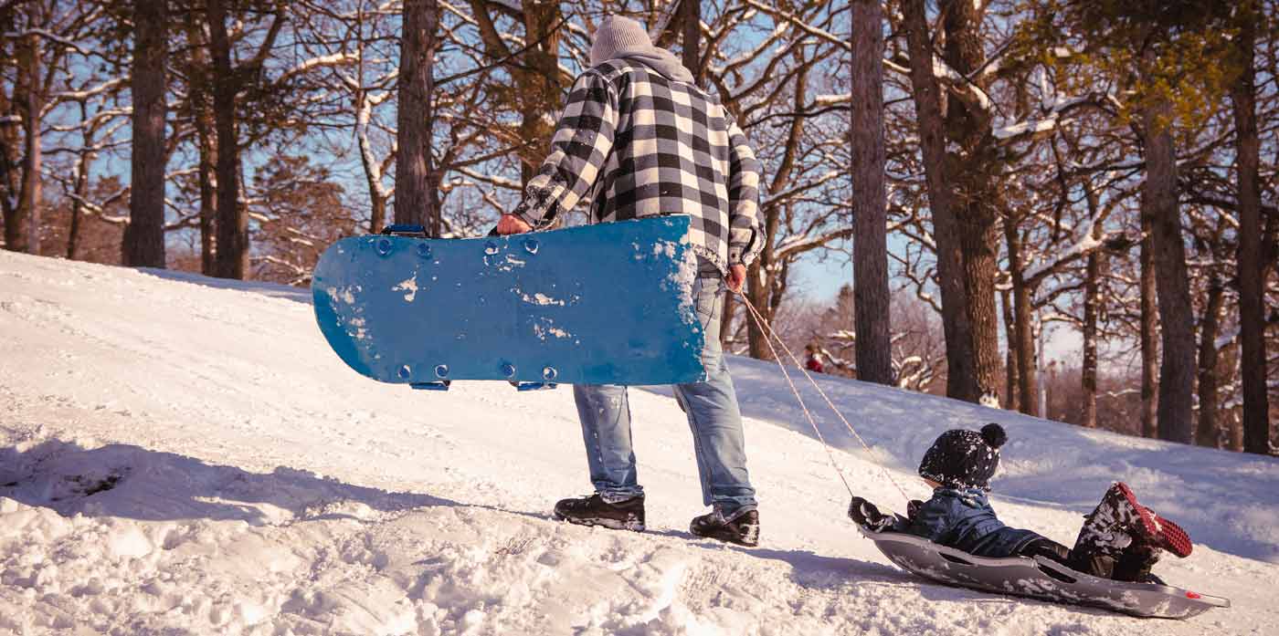 dad pulling his small child up a sledding hill
