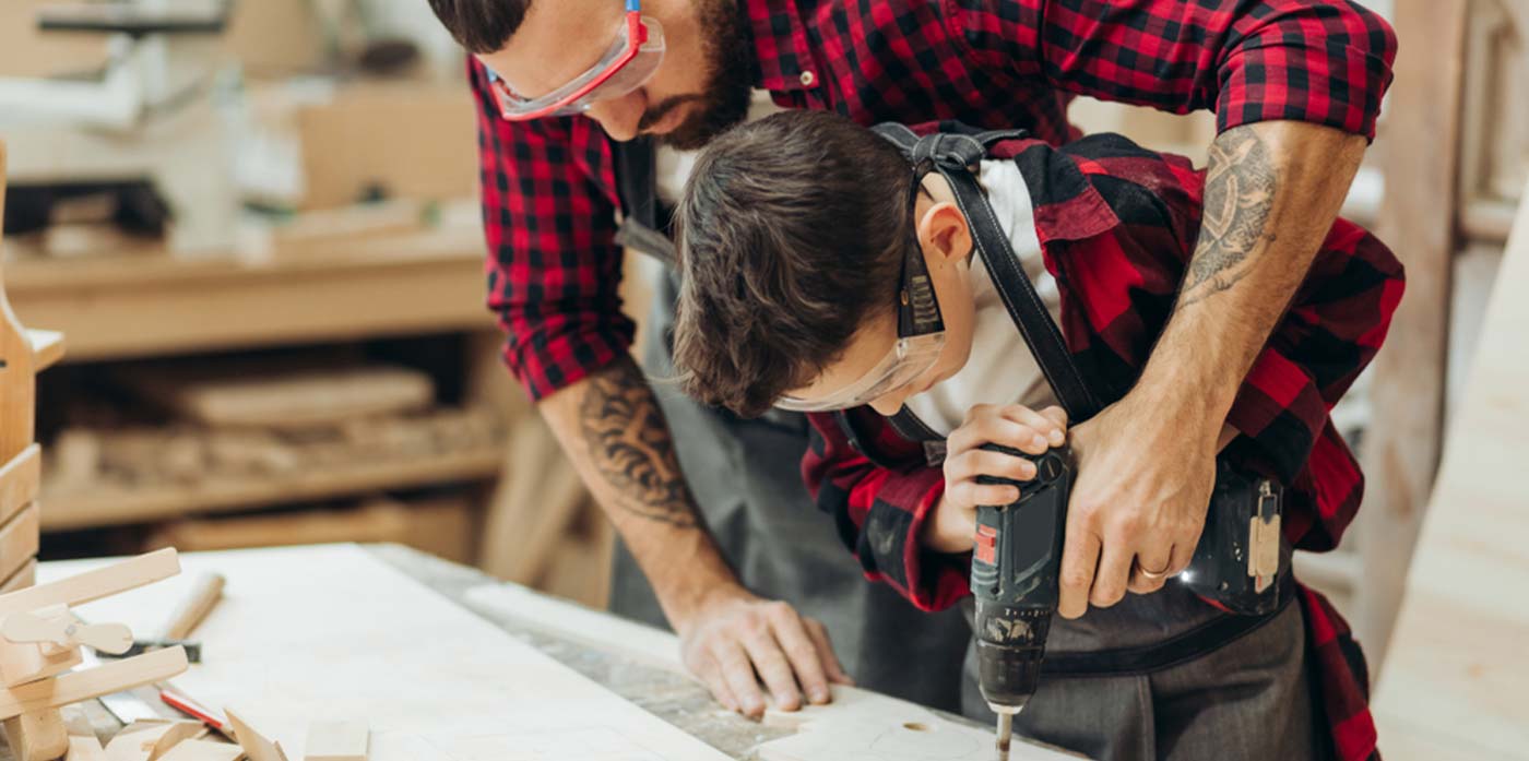 father teaching son how to use a drill in his business workshop