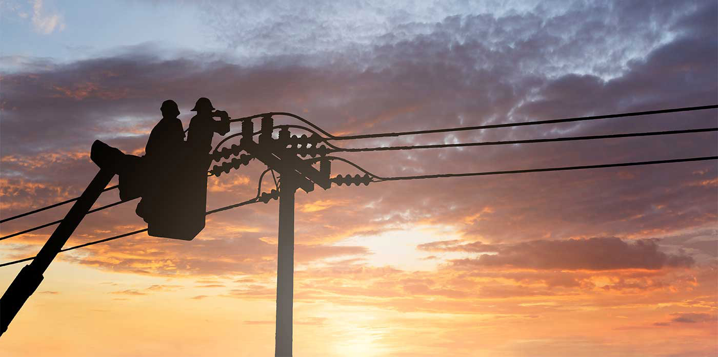 bucket lifting lineman to work on a power line, silhouetted against sunset