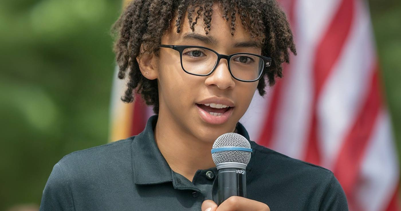 young person speaking in front of the american flag