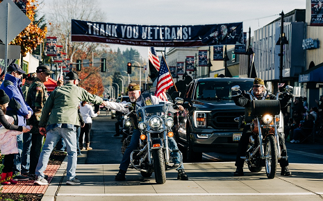 The image shows motorcyclists and spectators along Main Street during the annual Veterans Day Parade in Auburn, Washington.