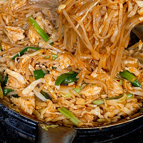 The image shows a freshly tossed pan of Pad Thai with rice noodles, scrambled egg, green onions, and bean sprouts.