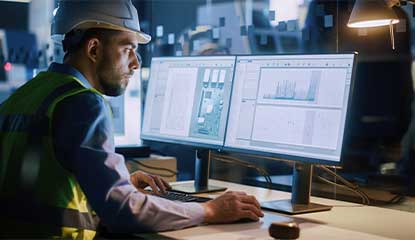 engineer in a hard hat looking at monitors