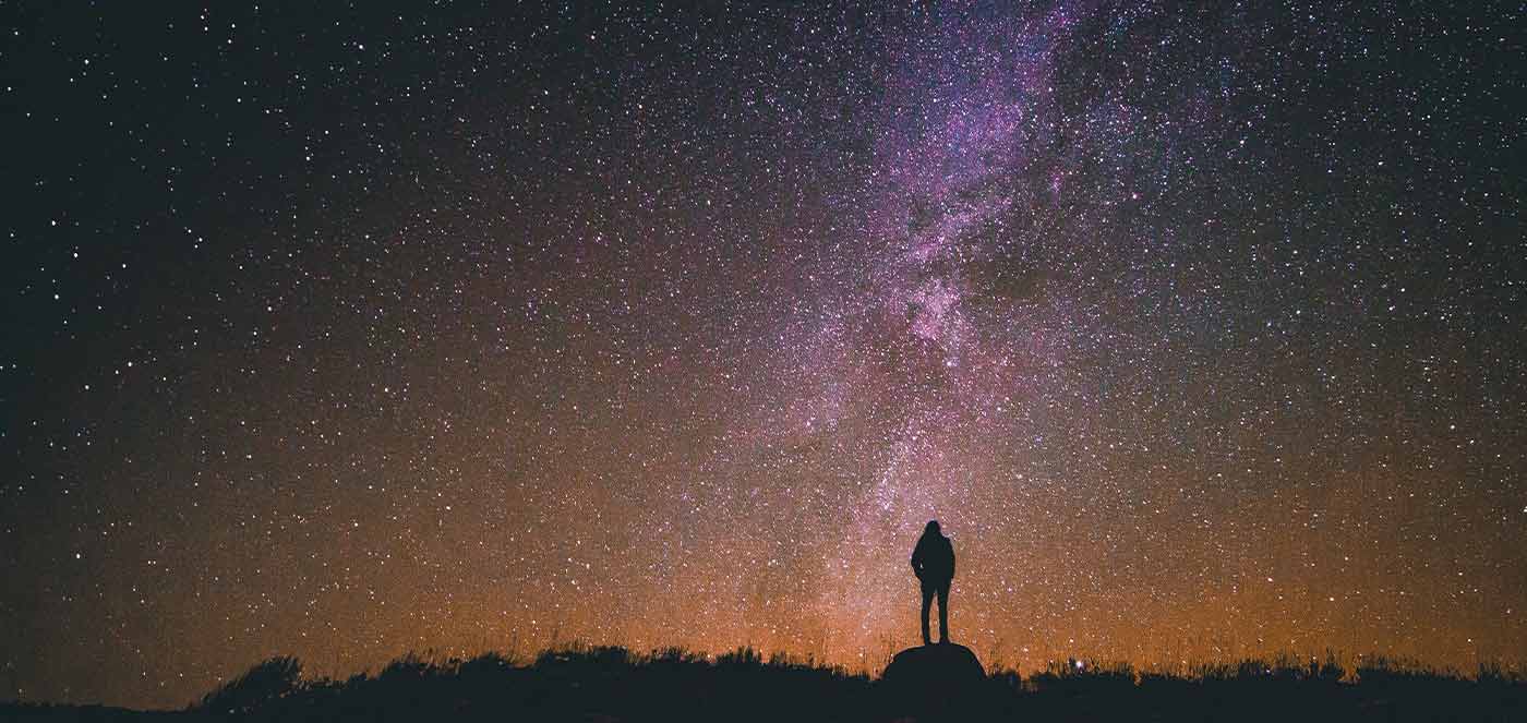 person standing on rock below the milky way sky