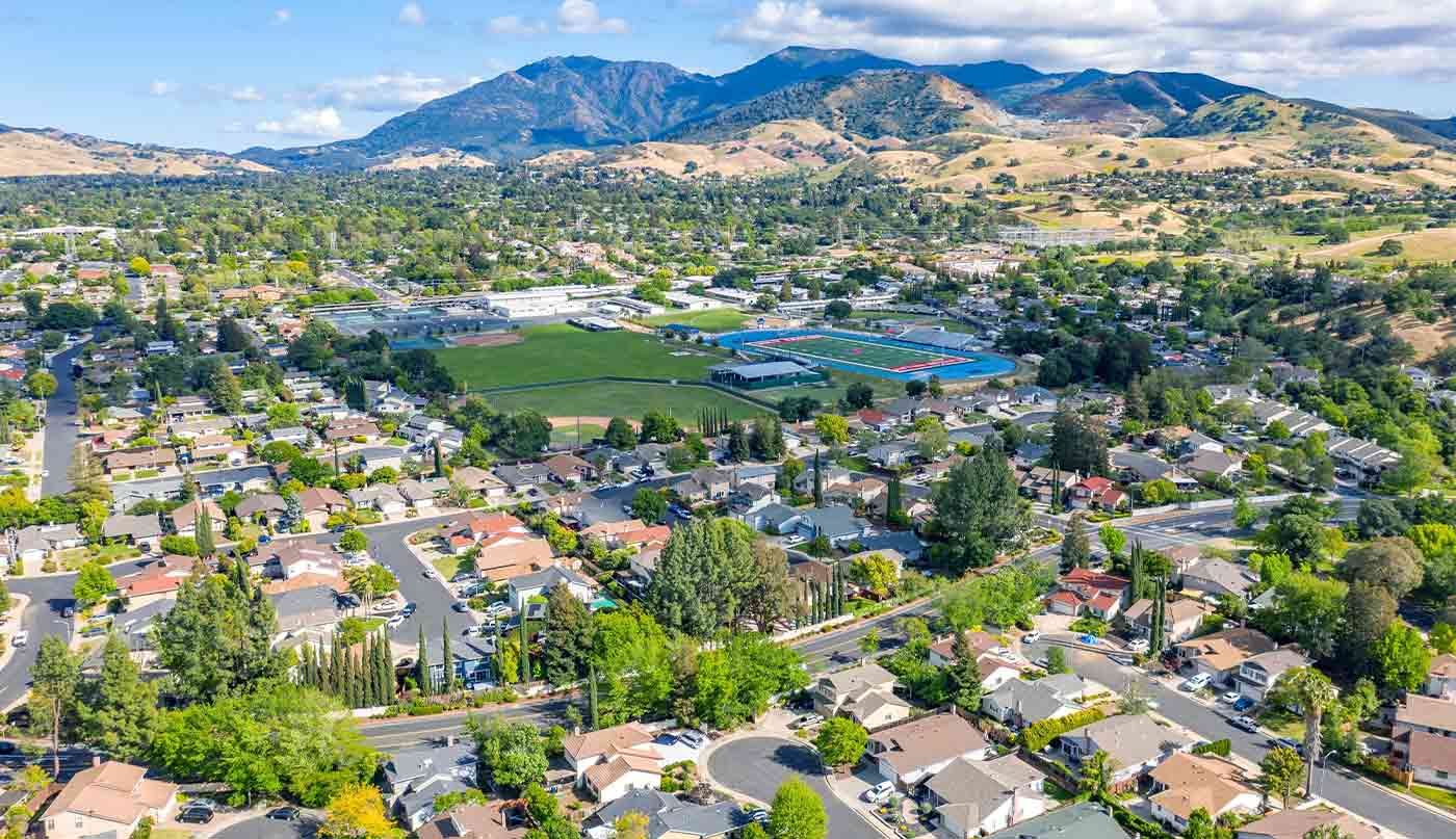 Aerial photo over the city of Concord, California with houses, green trees in the foreground and Mt.Diablo in the background