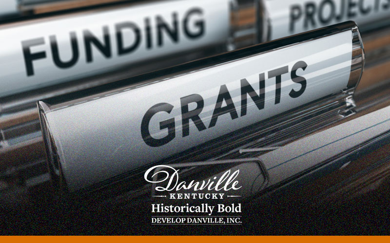The image shows a close-up view of brown hanging file folders in a drawer, with a prominent white tab labeled "Grants" in the foreground and other tabs labeled "Funding" and "Projects" behind it.