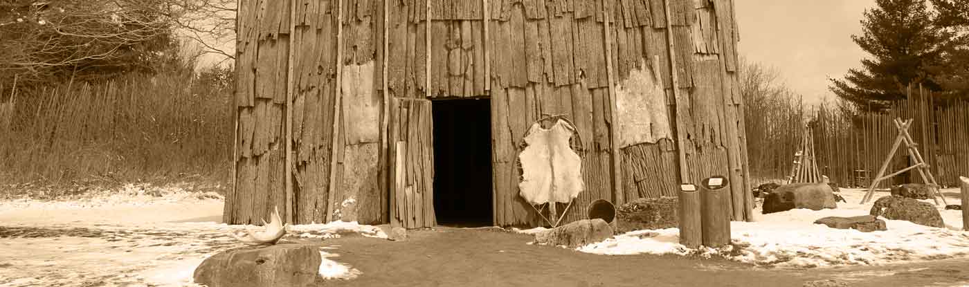 Image of an Iroquois longhouse with animal pelts and campfires outside of it.