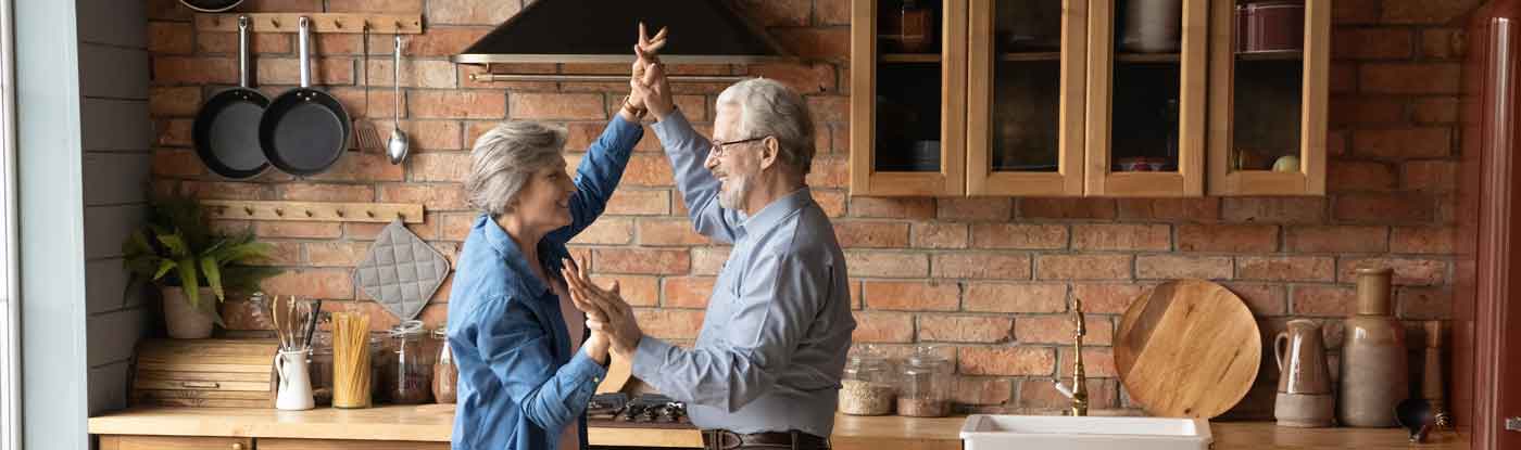 An older couple dance in the kitchen of a house