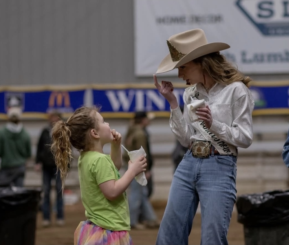 young woman in jeans and a cowboy hat interacting with a young girl